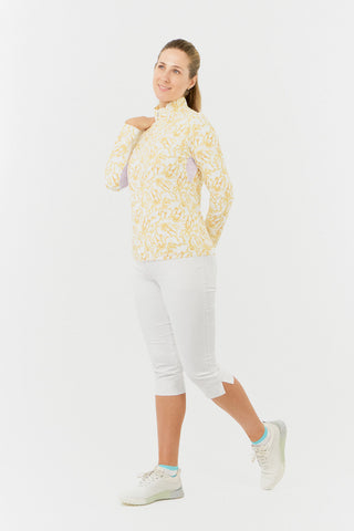 A side model shot of the Pure Golf Balance Sun Kissed Long Sleeve Ladies' Golf Zip Top from our Ray Flower collection features a beautiful print in warm honey hues. A regular fit and 4-way stretch, it ensures comfort for all body types. The mock neck collar adds a sleek look, while mesh sleeve panels enhance breathability. Made from 95% polyester and 5% spandex, it offers anti-crease, anti-static, and quick-dry properties, along with UPF 50+ protection. Paired with White Trust Capri's for a finished look.
