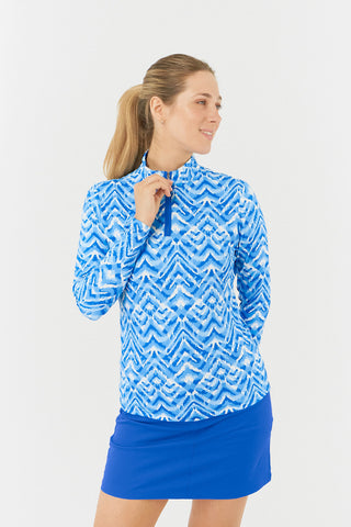 The close-up shot of the model in the Pure Golf Balance Santorini Skies Long Sleeve Ladies' Golf Zip Top features a mesmerizing Ikat-inspired design in shades of blue and white. With a regular fit and 4-way stretch, it provides comfort for all body types. The sleek mock neck collar adds style, while the mesh inside sleeve and underarm panels in Royal Blue enhance breathability. Crafted from 95% polyester and 5% spandex, it offers anti-crease, anti-static, and quick-dry properties, along with UPF 50+.